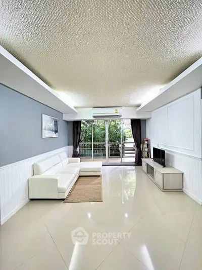 Spacious living room with modern decor and large windows opening to a lush balcony view.