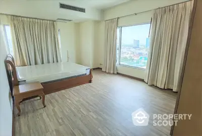 Spacious bedroom with large windows offering panoramic city views, ample natural light, and elegant floor-to-ceiling drapes in a high-rise apartment.