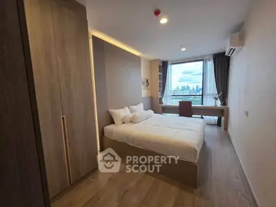 Modern bedroom with city view, featuring a cozy bed, wooden flooring, and a large window for natural light.