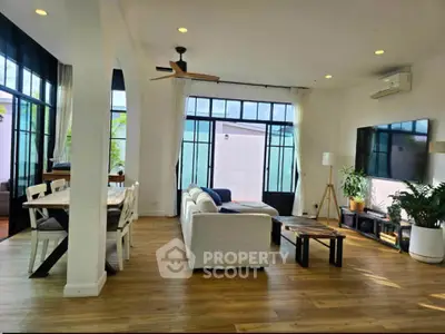 Spacious modern living room with large windows, wooden flooring, and stylish furniture.