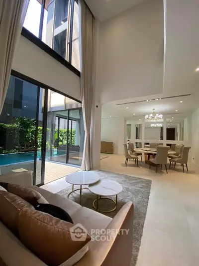 Luxurious open-plan living room with pool view, high ceilings, and elegant dining area in modern home.