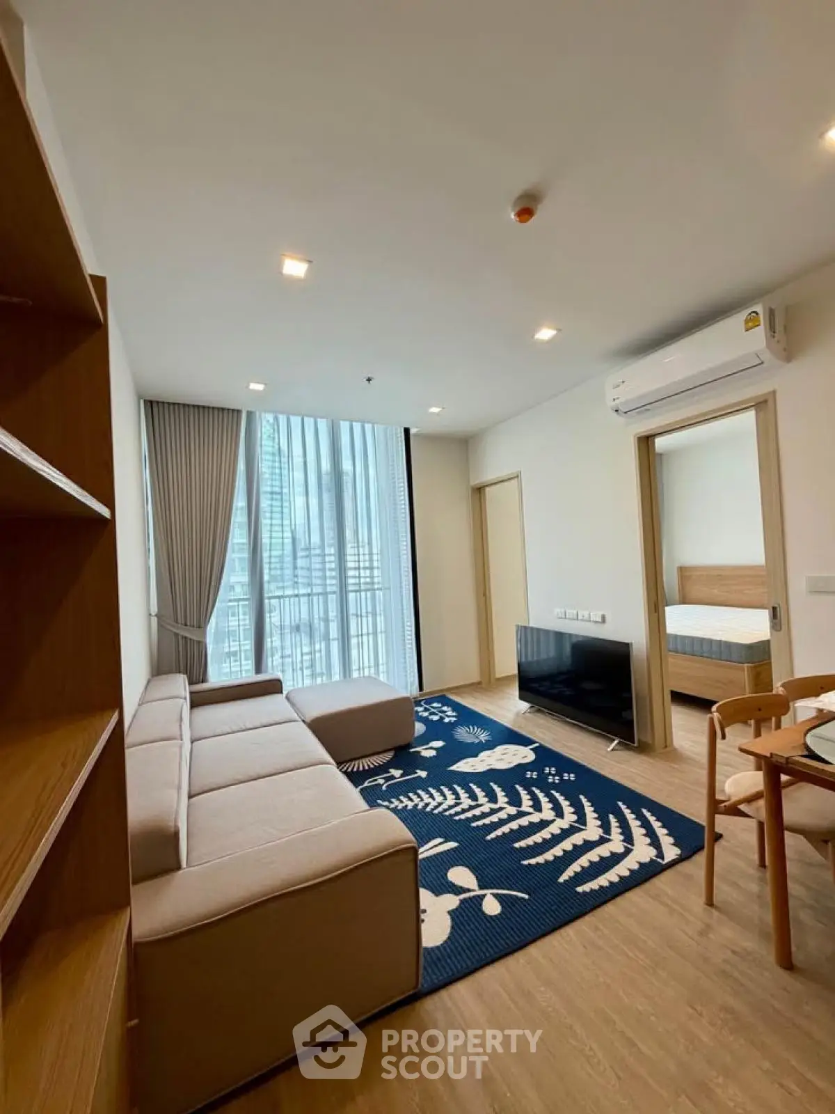 Modern living room with cozy sofa, stylish rug, and large window offering city views in a contemporary apartment.