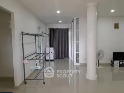 Spacious modern living area with sleek flooring and minimalist decor, featuring a fan and TV setup.