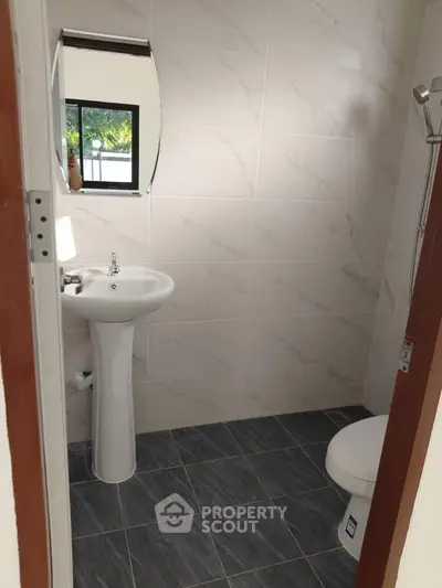 Modern bathroom with pedestal sink and tiled walls, featuring a sleek mirror.