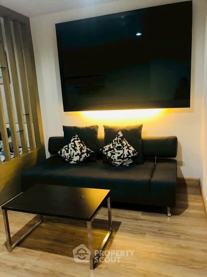 Modern living room with sleek black sofa, stylish cushions, and large wall-mounted TV.