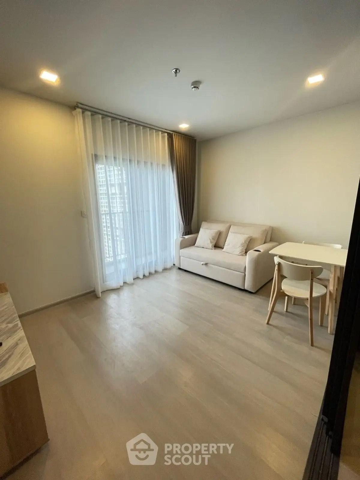 Modern living room with cozy sofa and dining set, featuring elegant curtains and wooden flooring.