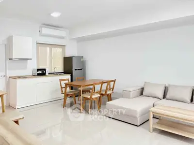 Modern open-plan living room with kitchen, dining area, and cozy sofa in a bright, minimalist design.