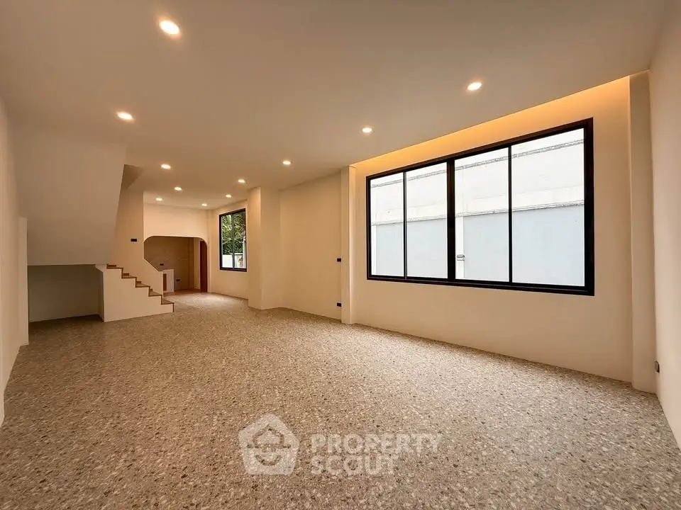 Spacious modern living room with large windows and elegant staircase, perfect for family gatherings.