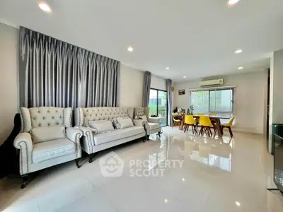 Spacious modern living room with elegant sofas and dining area, featuring large windows and bright lighting.