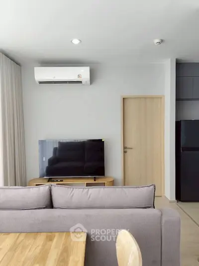 Modern living room with sleek furniture and air conditioning, featuring a flat-screen TV and minimalist decor.