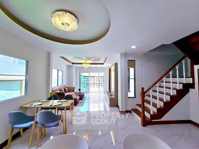 Spacious modern living room with elegant staircase and dining area, featuring stylish lighting and large windows.