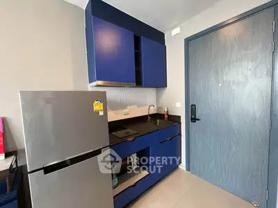 Modern compact kitchen with blue cabinets and stainless steel fridge in a stylish apartment.