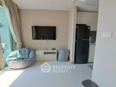 Modern living room with sleek TV setup and cozy seating, adjacent to a compact kitchen area.