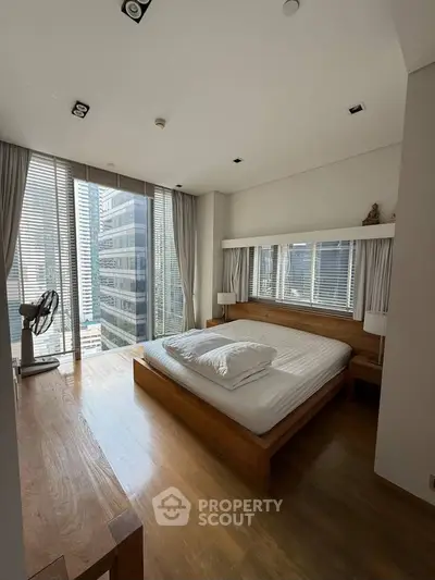 Modern bedroom with large windows and wooden furniture in a high-rise apartment.