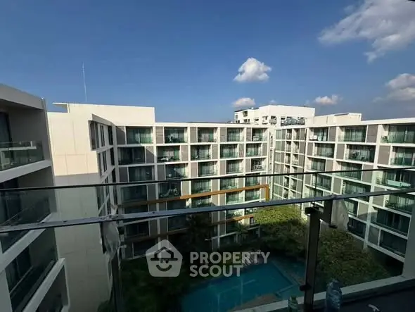 Modern apartment complex with pool view from balcony under clear blue sky.