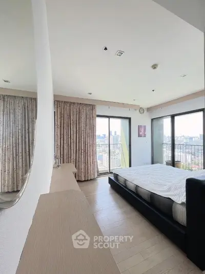 Spacious bedroom with city view and large windows, modern decor and natural light.