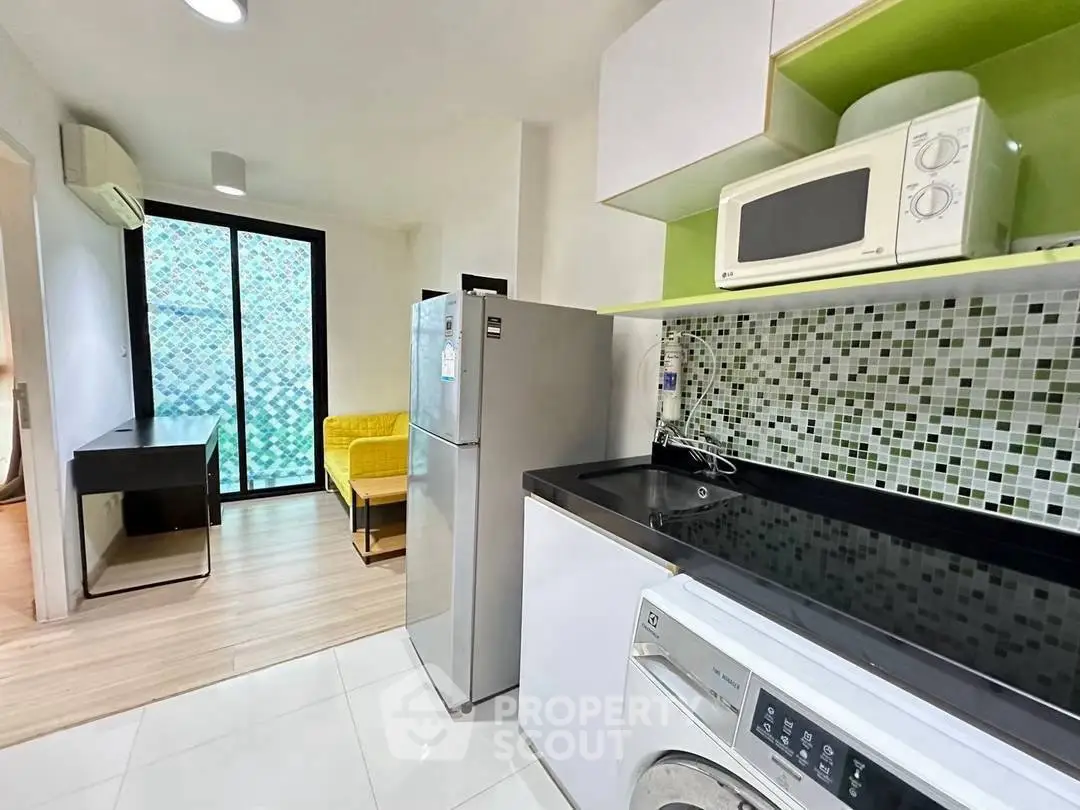Modern kitchen with mosaic backsplash, washing machine, and microwave in a compact apartment.