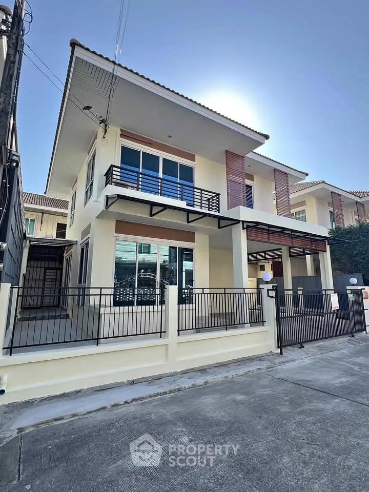 Modern two-story house with balcony and gated entrance in a suburban neighborhood.
