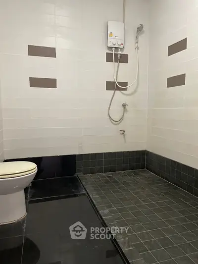Modern bathroom with sleek black tiles and shower area, featuring a water heater for comfort.