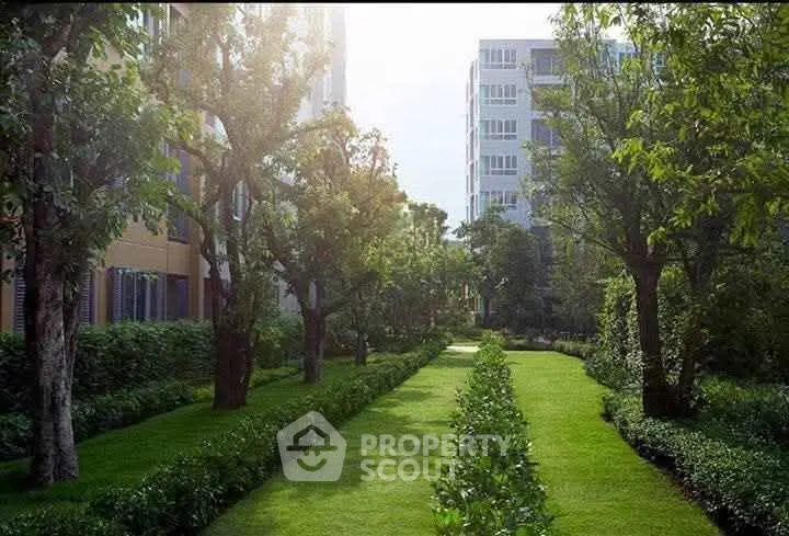 Lush green garden with trees and modern apartment buildings in the background, perfect for serene living.