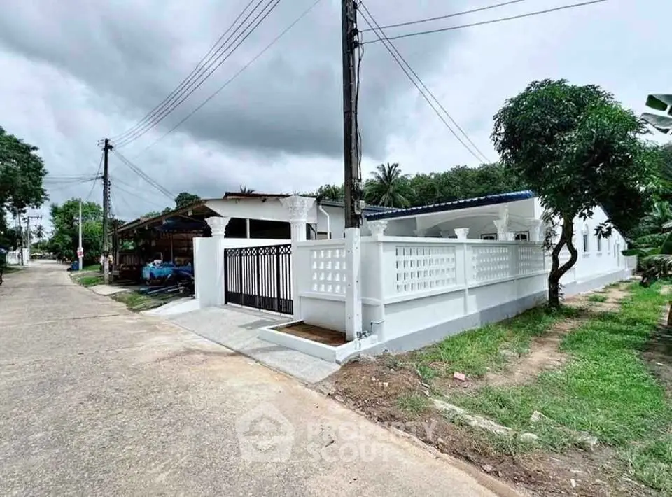 Charming white-walled house with spacious yard and lush greenery in serene neighborhood.