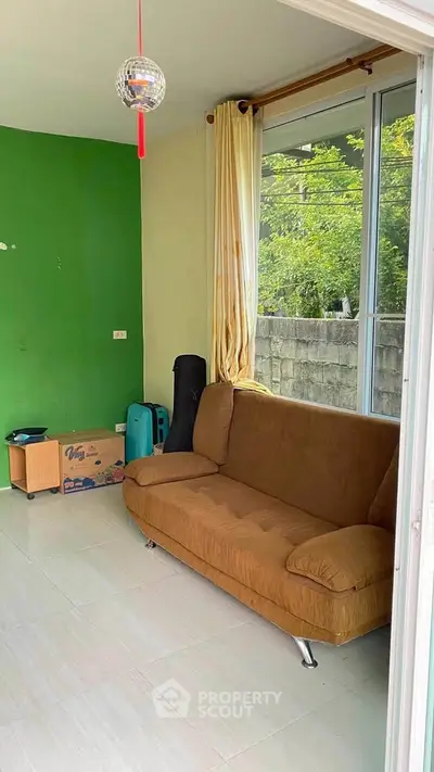 Cozy living room with brown sofa and green accent wall, large window view