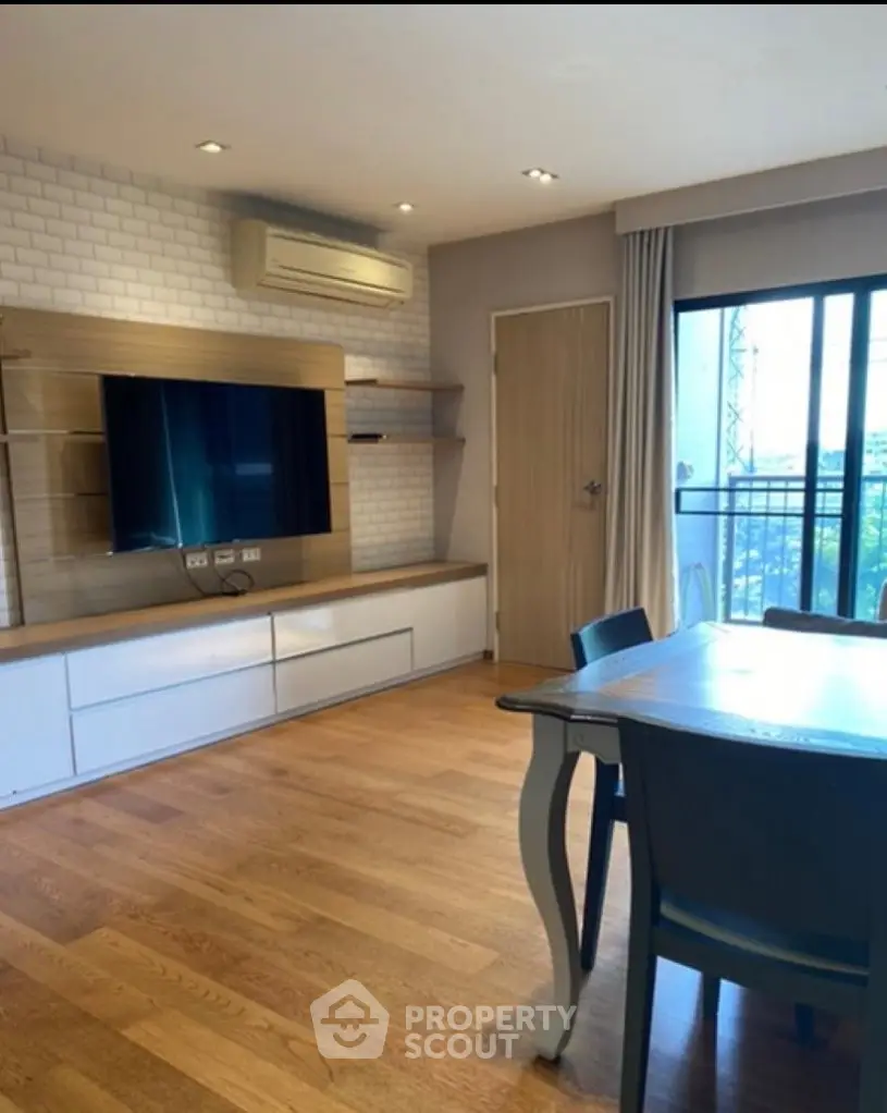 Modern living room with wooden flooring, stylish TV unit, and balcony view.
