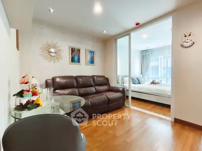 Stylish living room with leather sofa and glass table, adjacent to a cozy bedroom with natural light.
