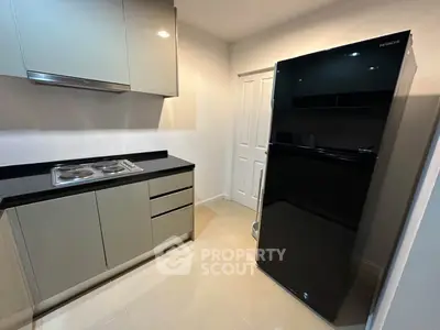 Modern kitchen with sleek cabinetry and black fridge, featuring a compact electric stove.