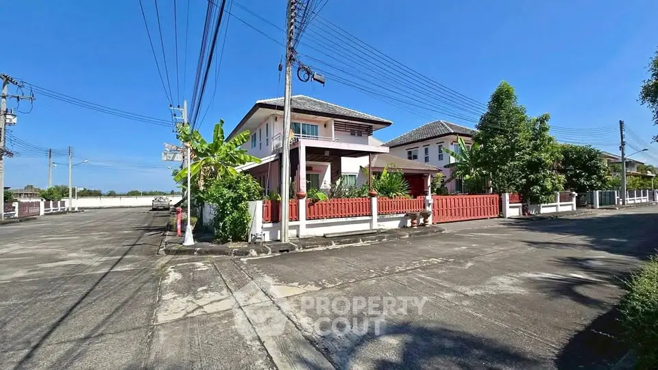 Charming two-story house with red fence and lush greenery on a sunny day.