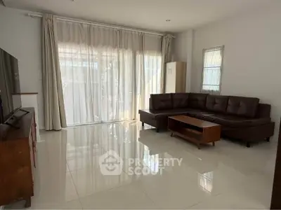 Spacious living room with modern brown leather sofa and large windows for natural light.