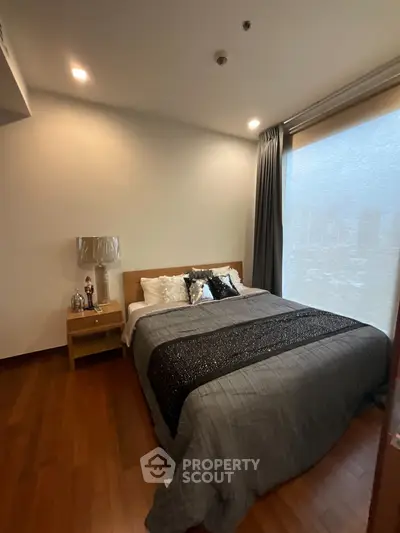 Cozy bedroom with wooden flooring and large window, featuring a comfortable bed and stylish decor.