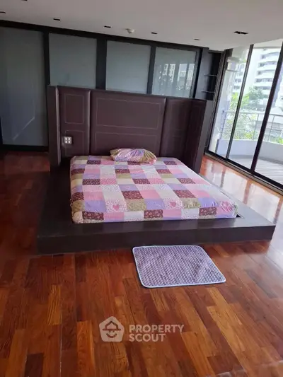 Spacious bedroom with wooden flooring and large windows offering natural light and city views.
