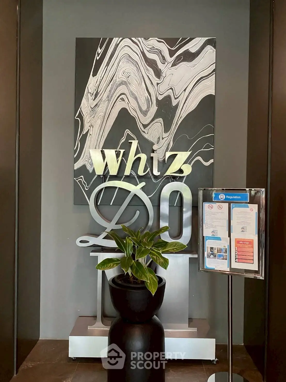 Modern building entrance with stylish decor and signage, featuring a sleek plant arrangement.