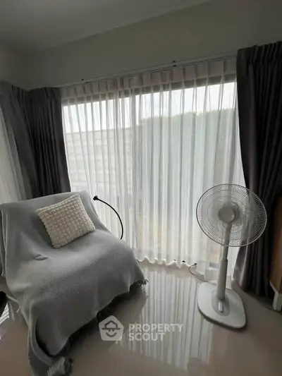 Cozy living room corner with armchair and fan by large window