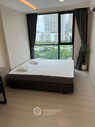 Modern bedroom with large window offering city view, featuring a comfortable bed and stylish decor.