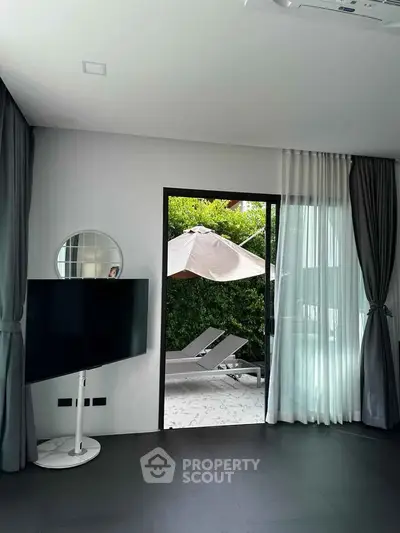 Modern living room with sleek TV stand and view of outdoor patio with lounge chairs and umbrella.