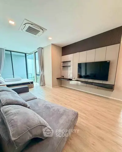 Spacious modern living room with large TV and cozy seating area, featuring floor-to-ceiling windows.