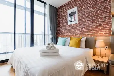 Chic urban bedroom with exposed brick wall, large windows offering ample natural light, and tasteful decor creating a cozy atmosphere.