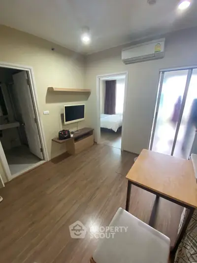 Cozy living room with wooden flooring, wall-mounted TV, and air conditioning in modern apartment.