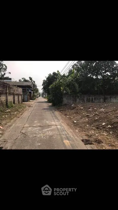 Quiet suburban street with potential for development, featuring open land and residential buildings.