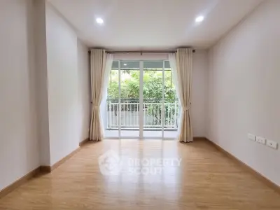Spacious empty room with wooden flooring and large window overlooking greenery.