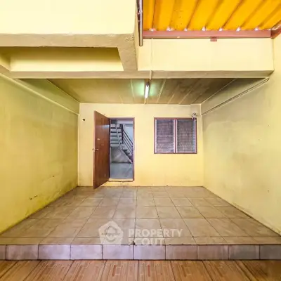 Spacious interior room with tiled flooring and yellow walls, featuring a wooden door and window.