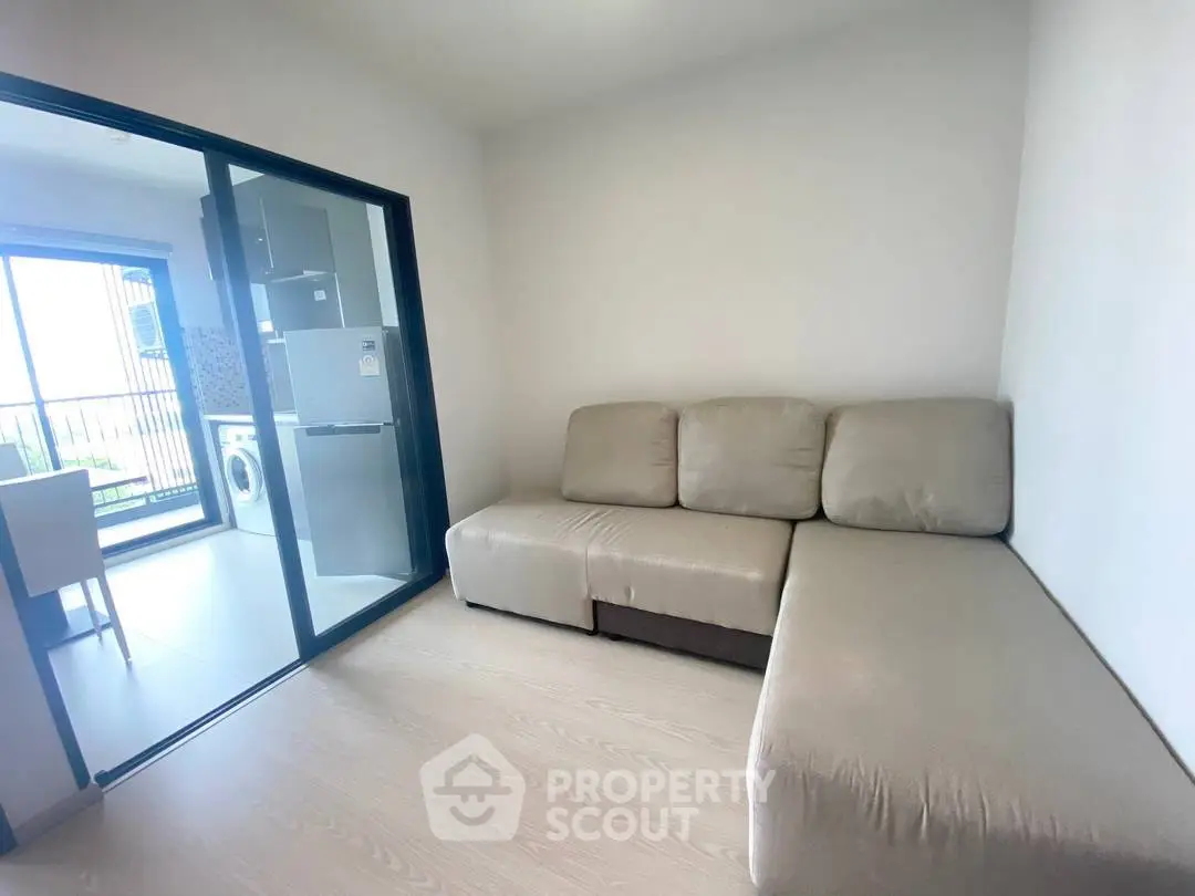 Modern living room with beige sofa and glass sliding door leading to kitchen area.
