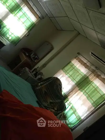 Cozy bedroom with colorful curtains and ceiling tiles, featuring a comfortable bed and air conditioning.