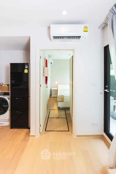 Modern apartment interior with wooden flooring, air conditioning, and a view into a cozy bedroom.