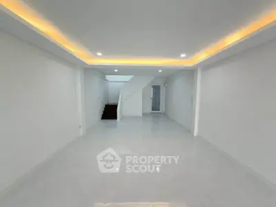 Spacious modern living room with sleek white tiles and ambient ceiling lighting.