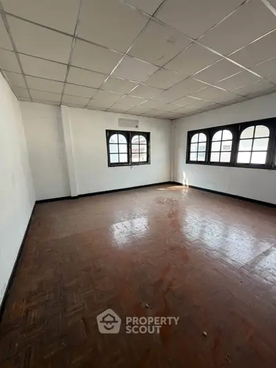 Spacious empty room with parquet flooring and arched windows, ideal for customization.