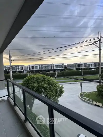 Modern balcony with glass railing overlooking a serene suburban street and lush greenery.