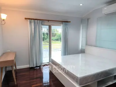 Bright bedroom with large window and balcony access, featuring hardwood floors and modern furnishings.